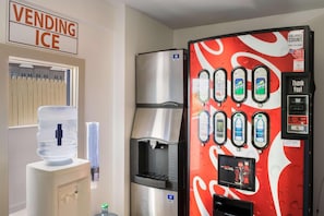Máquina automática com logotipo da Coca-Cola, um dispensador de água e um aviso que diz 'VENDENDO GELO'.