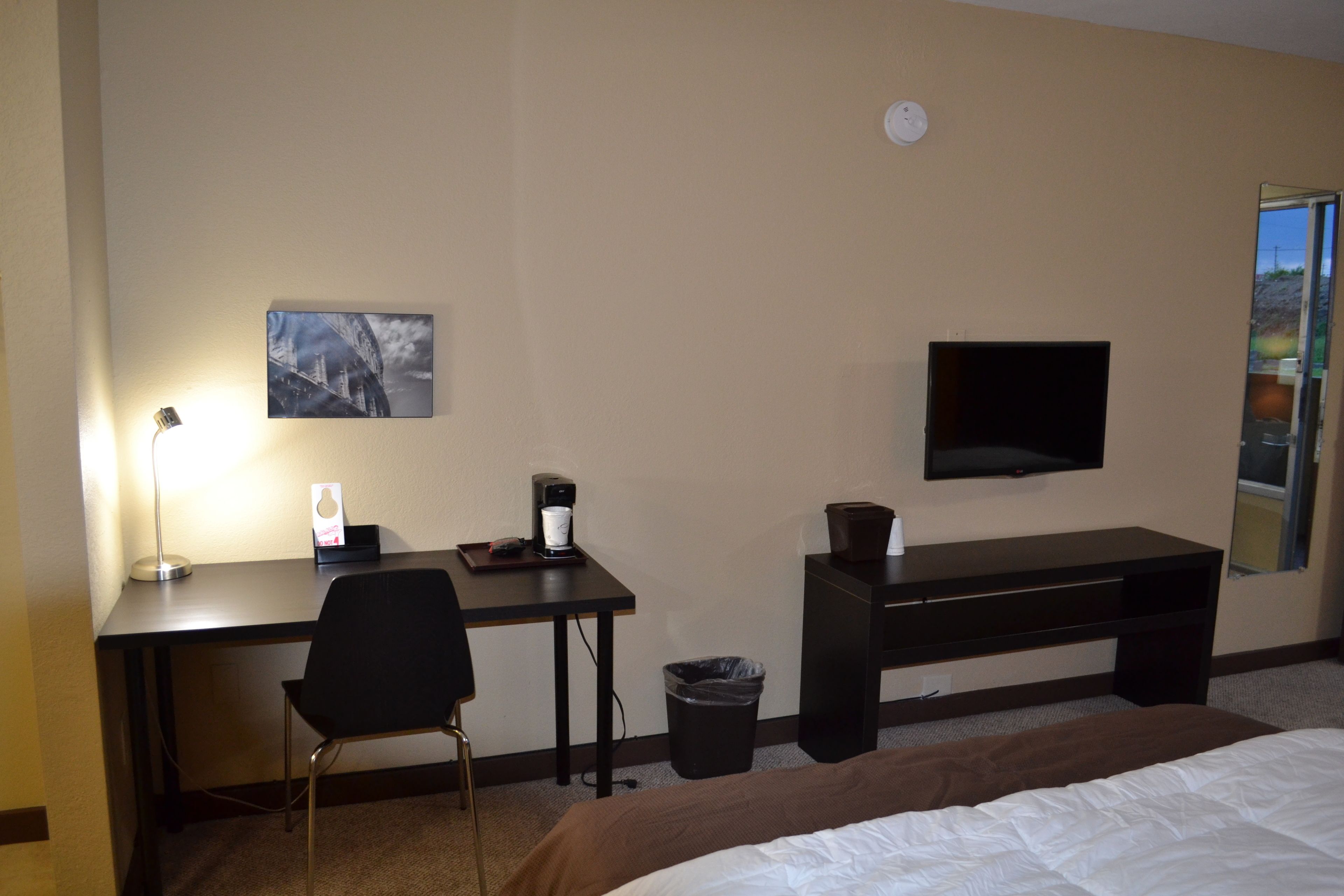 A hotel room with a bed, a desk with a chair, a TV, a coffee maker, and a trash can.