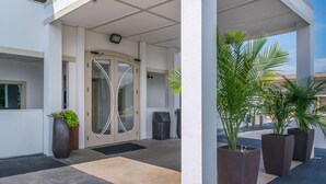 A hotel entrance with a glass door, a covered waiting area, and potted plants. - Motel 75 Monroe (Monroe)