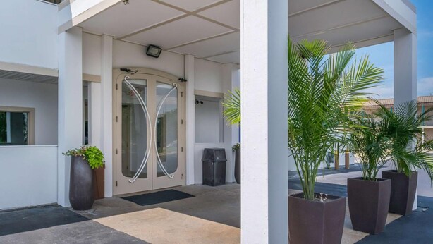 A hotel entrance with a glass door, potted plants, and a covered walkway. - Motel 75 Monroe (Monroe)