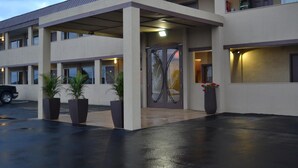 A hotel entrance with a covered walkway, potted plants, and a visible door with signage. - Motel 75 Monroe (Monroe)