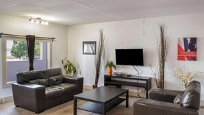 A living room with a brown leather sofa, a coffee table, a flat-screen TV, and decorative plants. - Motel 75 Monroe (Monroe)