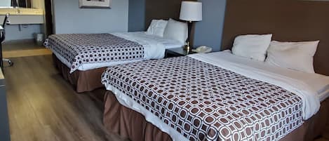 A hotel room with two beds, each with patterned bedding and brown skirts. There is a nightstand with a lamp, a framed picture on the wall, and a window with curtains.