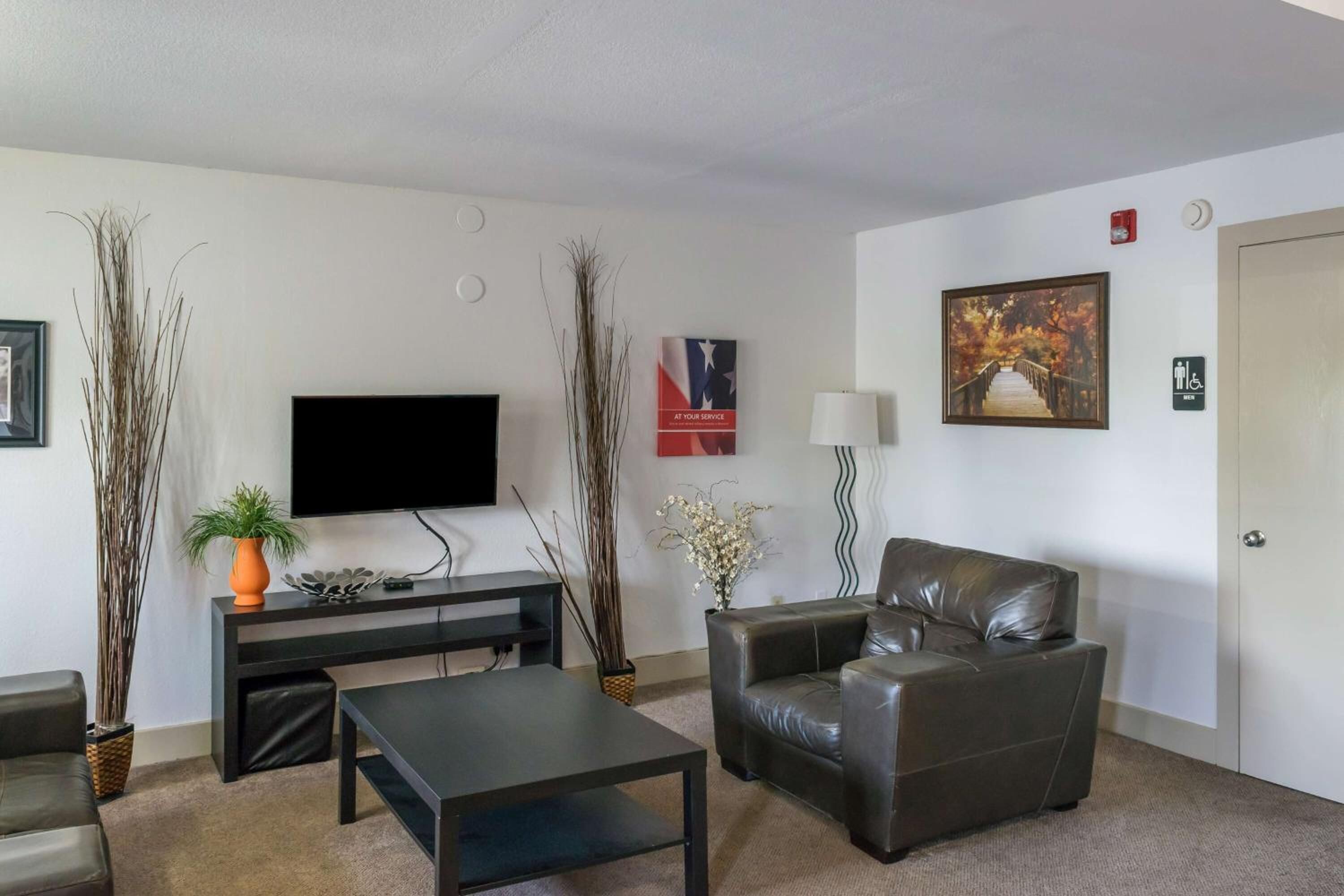 A living room with a flat-screen TV, leather sofa, coffee table, and decorative plants.
