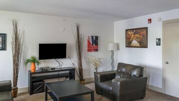 A living room with a flat-screen TV, leather sofa, coffee table, and decorative plants.