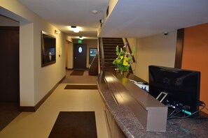 A hotel reception area with a reception desk, a clock, a staircase, and a security camera.