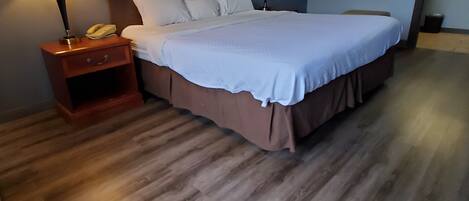 Una habitación de hotel con una cama grande, dos lámparas de noche, una mesita de noche de madera y un cuadro enmarcado en la pared.