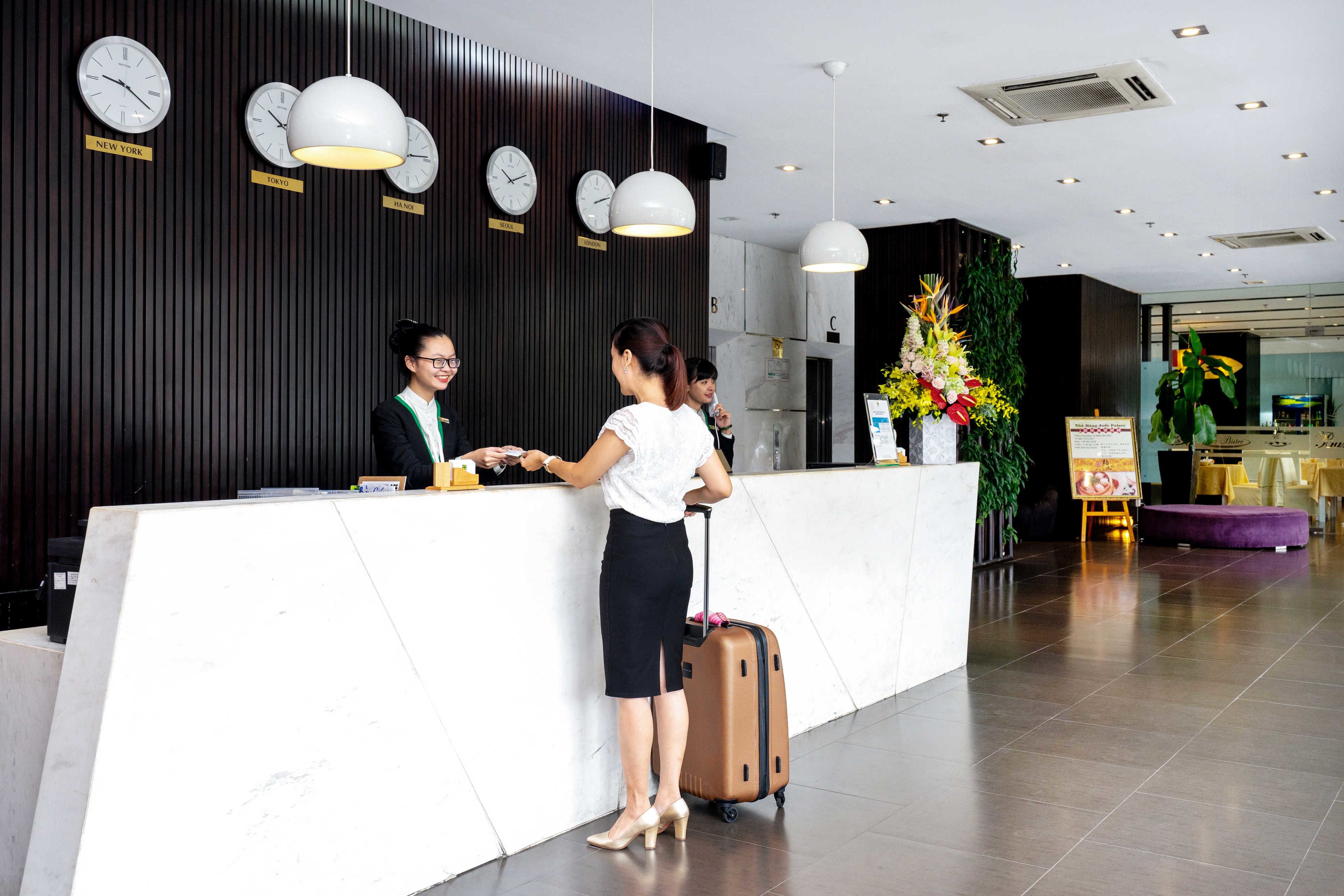 A reception desk with clocks labeled with city names, a large potted plant, and a check-in counter.