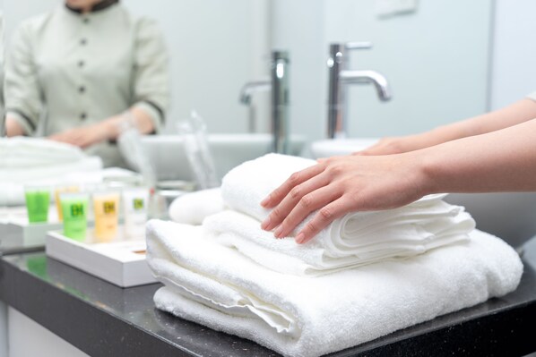 A stack of white towels on a black countertop with a person’s hand resting on them. - Becamex Hotel Thu Dau Mot (Ho Chi Minh City)