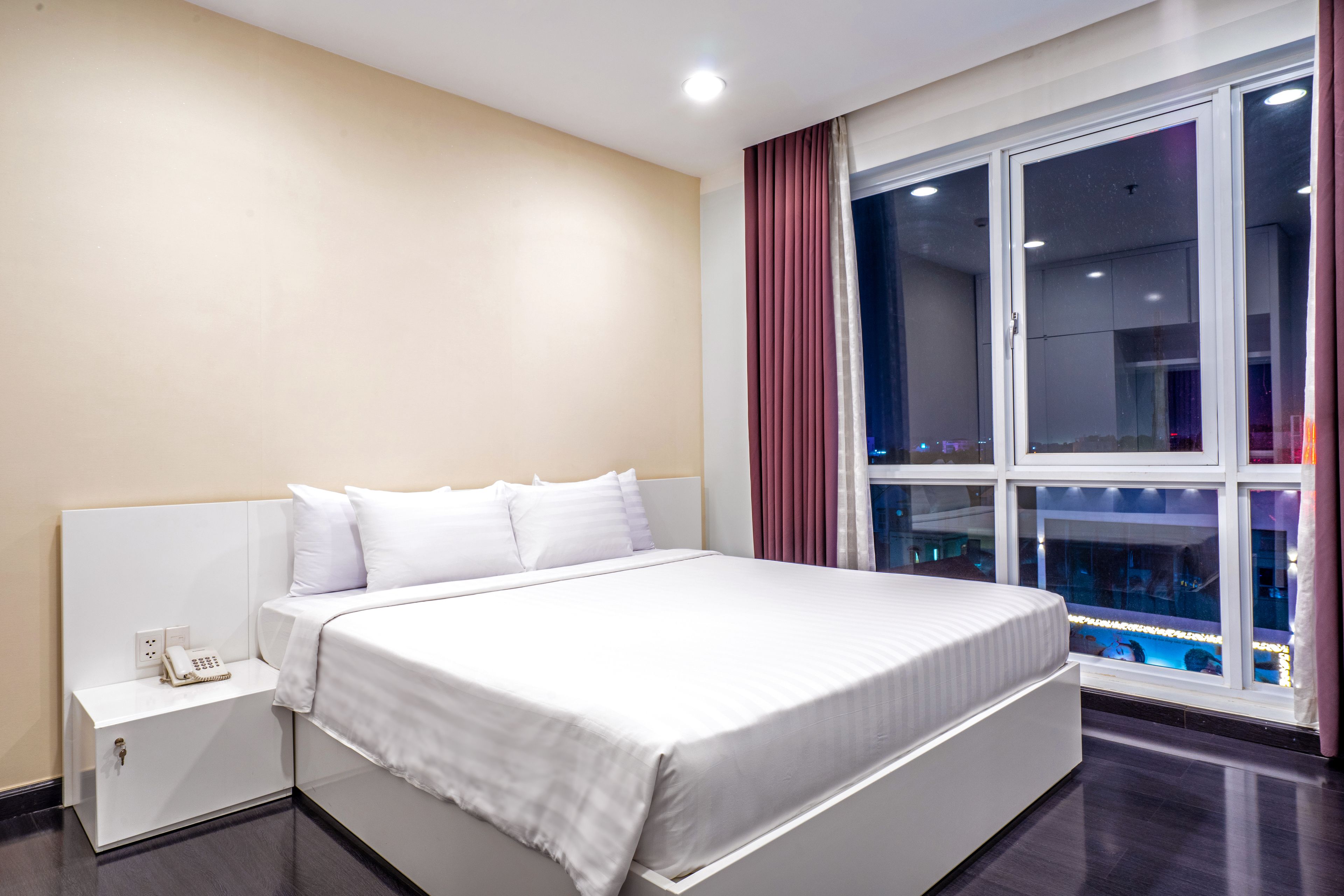 Ein modernes Hotelzimmer mit einem großen Bett, einem Nachttischtelefon und einem fensterbelaubten Fenster.