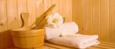 A wooden sauna with a wooden bucket, a wooden mallet, and a white towel with a flower.