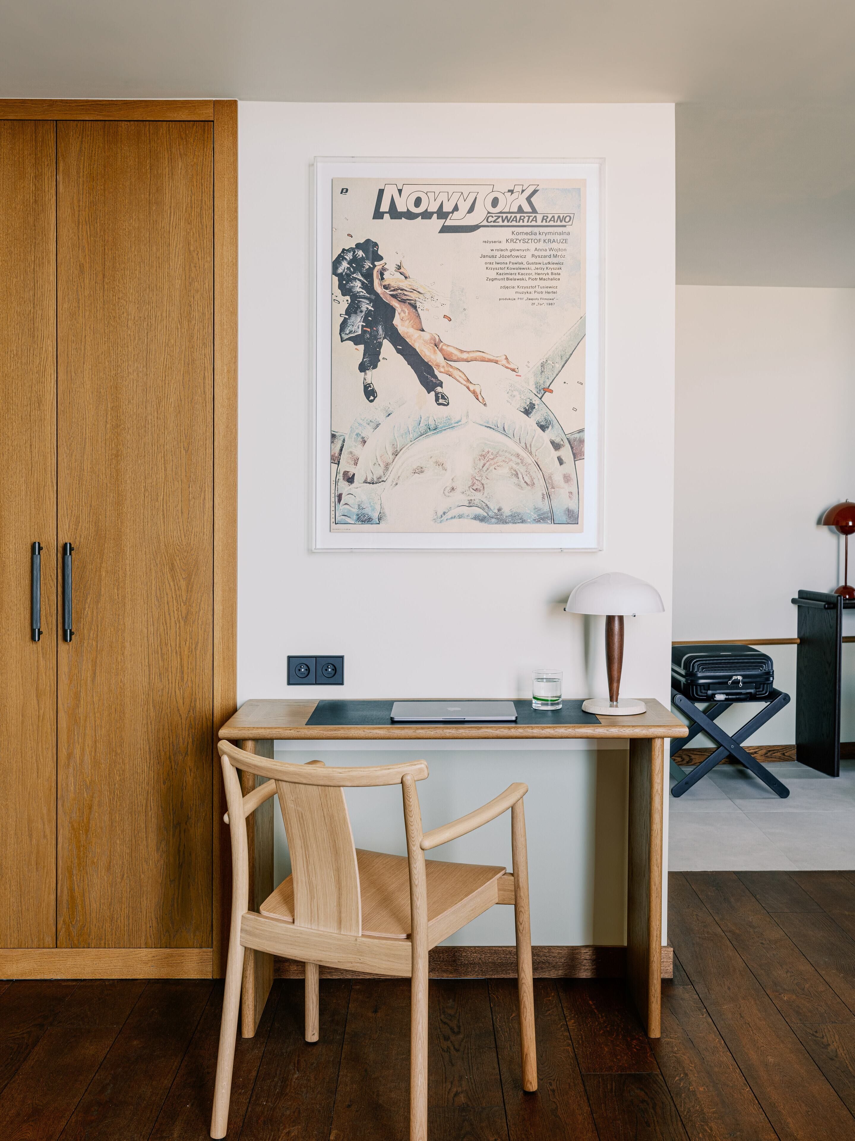 A small room with a wooden desk, a chair, a framed poster on the wall, and a wardrobe.