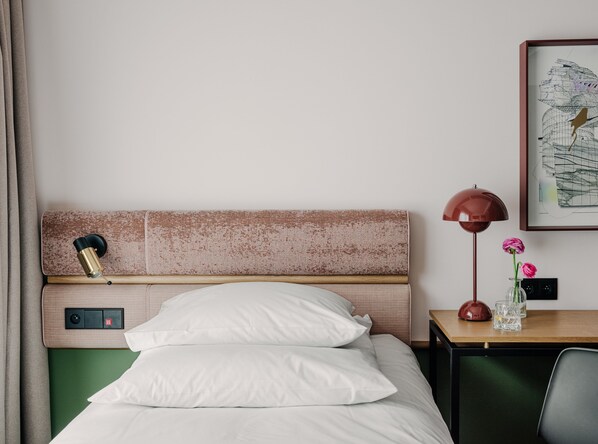 A neatly made bed with white linens, a headboard with a textured finish, a bedside table with a lamp, and a framed artwork on the wall.