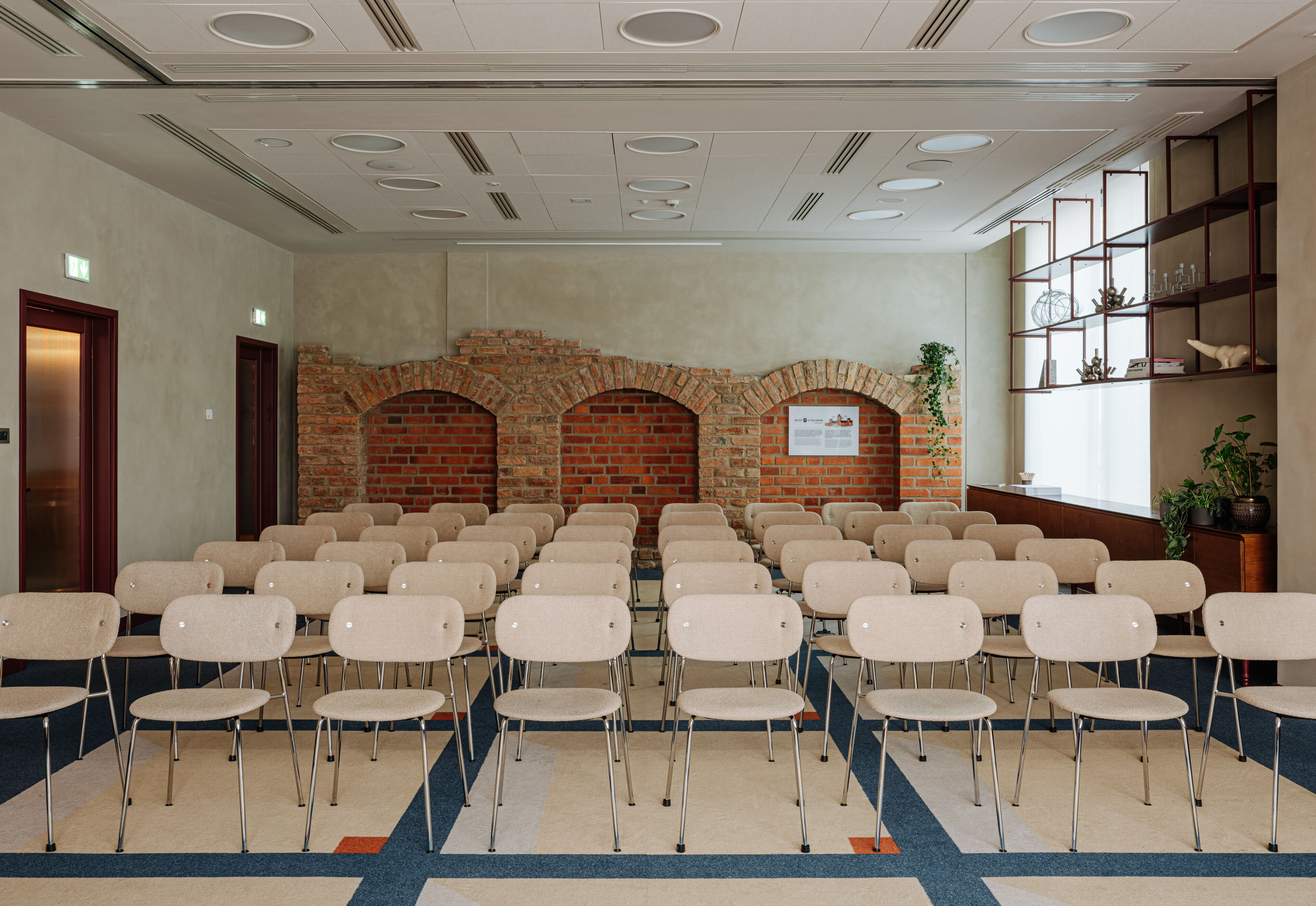 Een vergaderruimte met rijen stoelen, een bakstenen muur en een boekenkast.