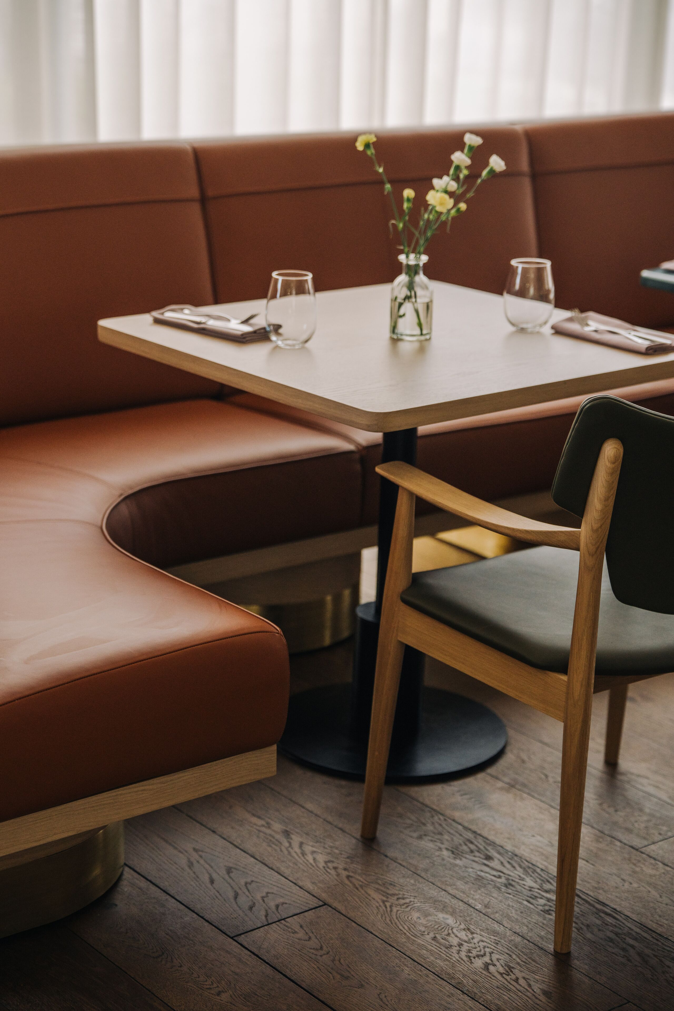 A dining area with a wooden table, a vase with flowers, and a cushioned bench.
