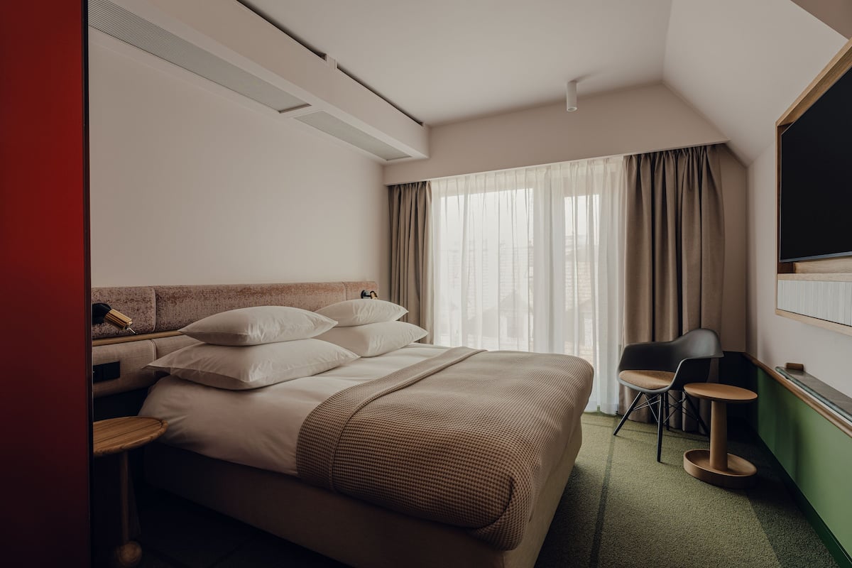Ein Hotelzimmer mit einem großen Bett, einem Schreibtisch, einem Sessel und einem Fernseher.