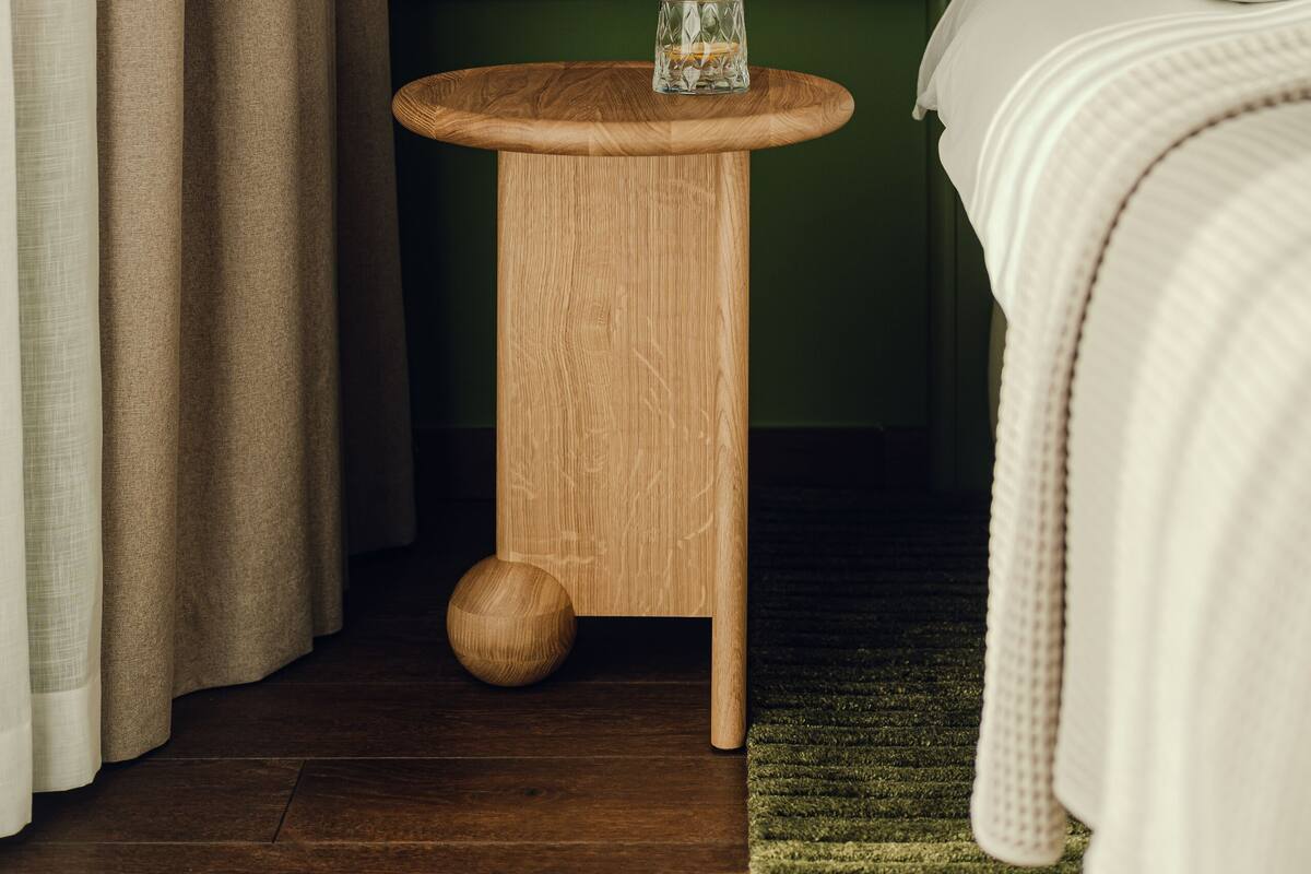 Ein ordentlich eingerichtetes Hotelzimmer mit einem Nachttisch aus Holz, einer Nachttischlampe und einem grünen Teppich.