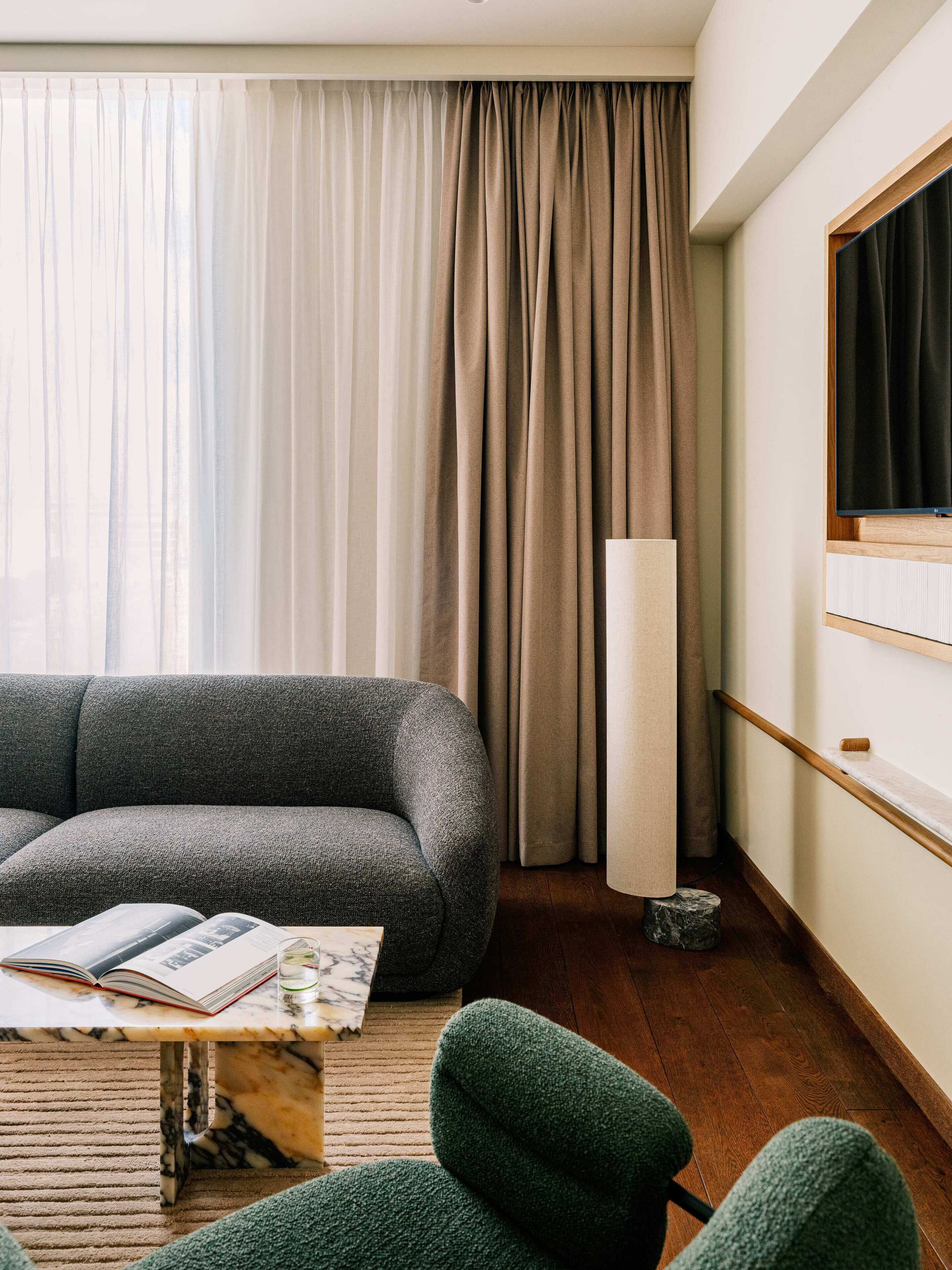 A modern living room with a grey sofa, a small table with a book and a glass, and a floor lamp.