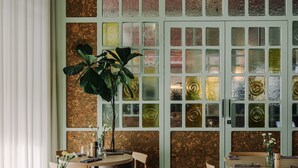 A restaurant with a round table and chairs, a large potted plant, and a wall with patterned glass windows. - PURO Poznań Stare Miasto (Poznan)