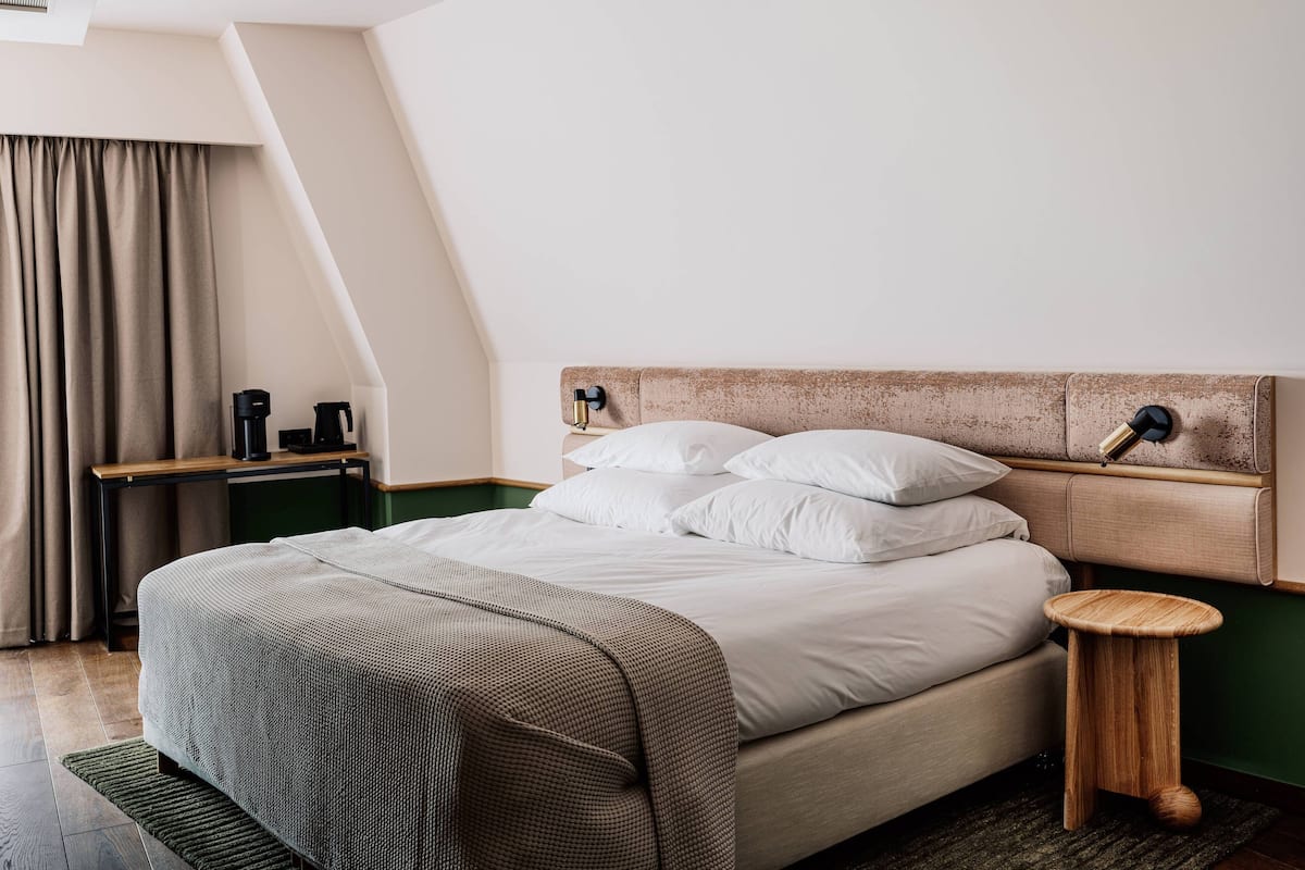 Ein modernes Hotelzimmer mit einem Bett, einem Nachttisch und einem kleinen Holzschemel.