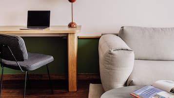 A workspace with a wooden desk, a laptop, a lamp, a chair, a sofa, and a small table with a book.