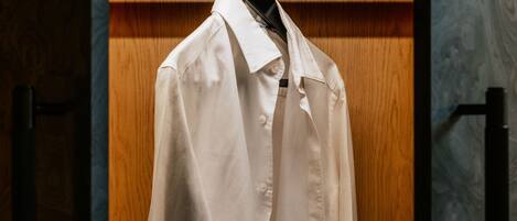A white shirt hanging on a wooden hanger in a closet with a wooden door and a marble-patterned wall.