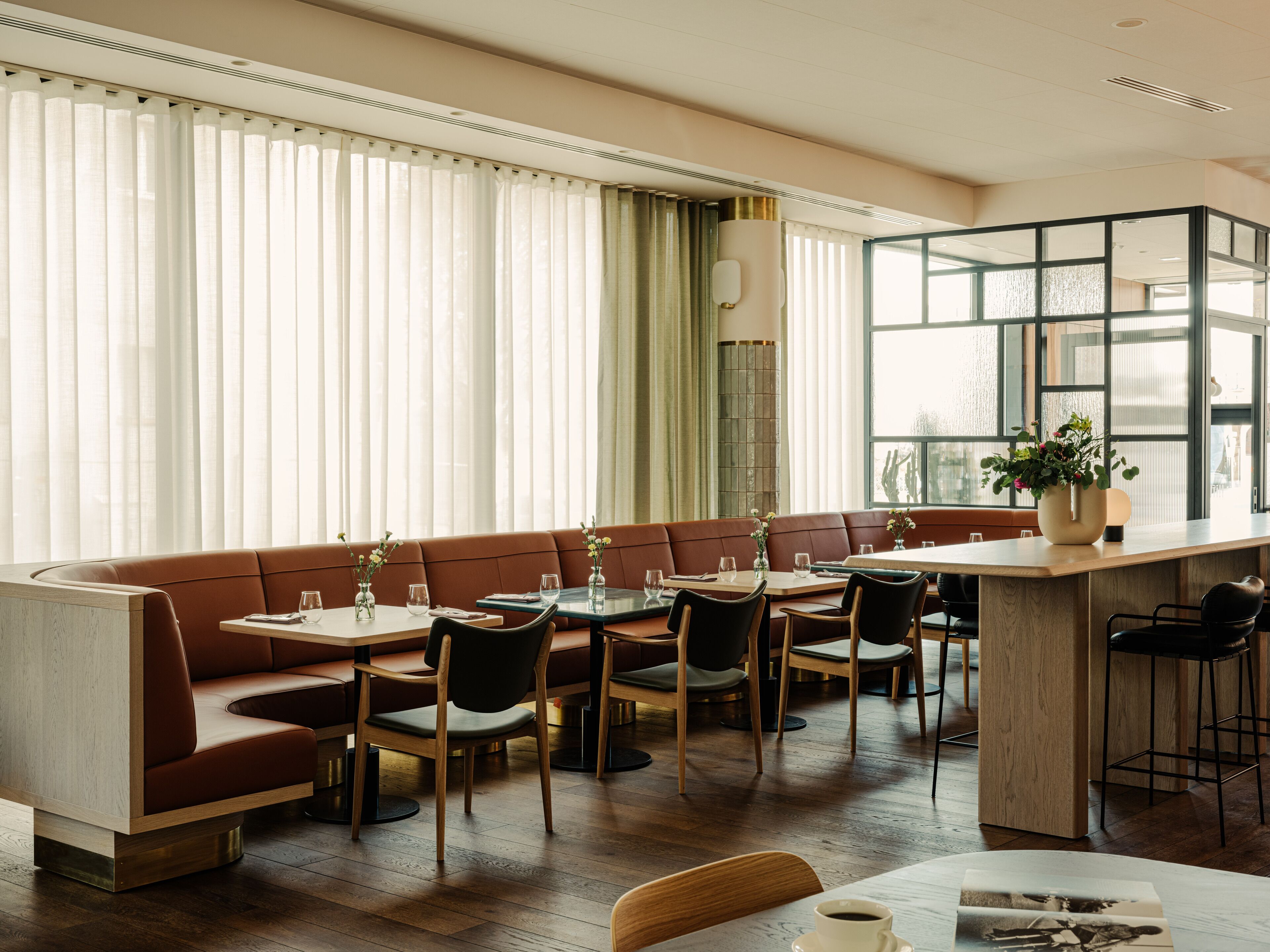 A modern dining area with a wooden bar, cushioned seating, and large windows.