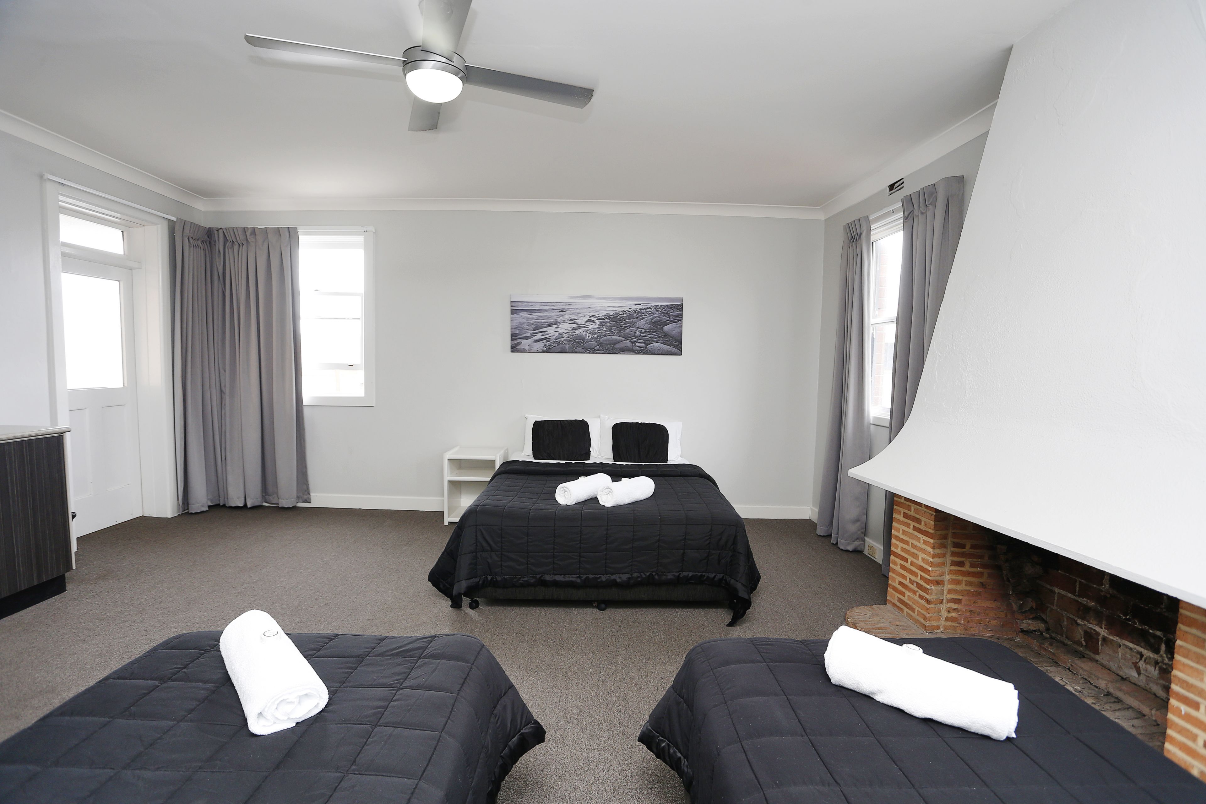 A hotel room with two beds, a ceiling fan, a fireplace, and a painting on the wall.