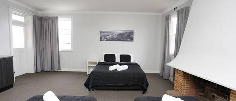 A hotel room with two beds, a ceiling fan, a fireplace, and a painting on the wall.