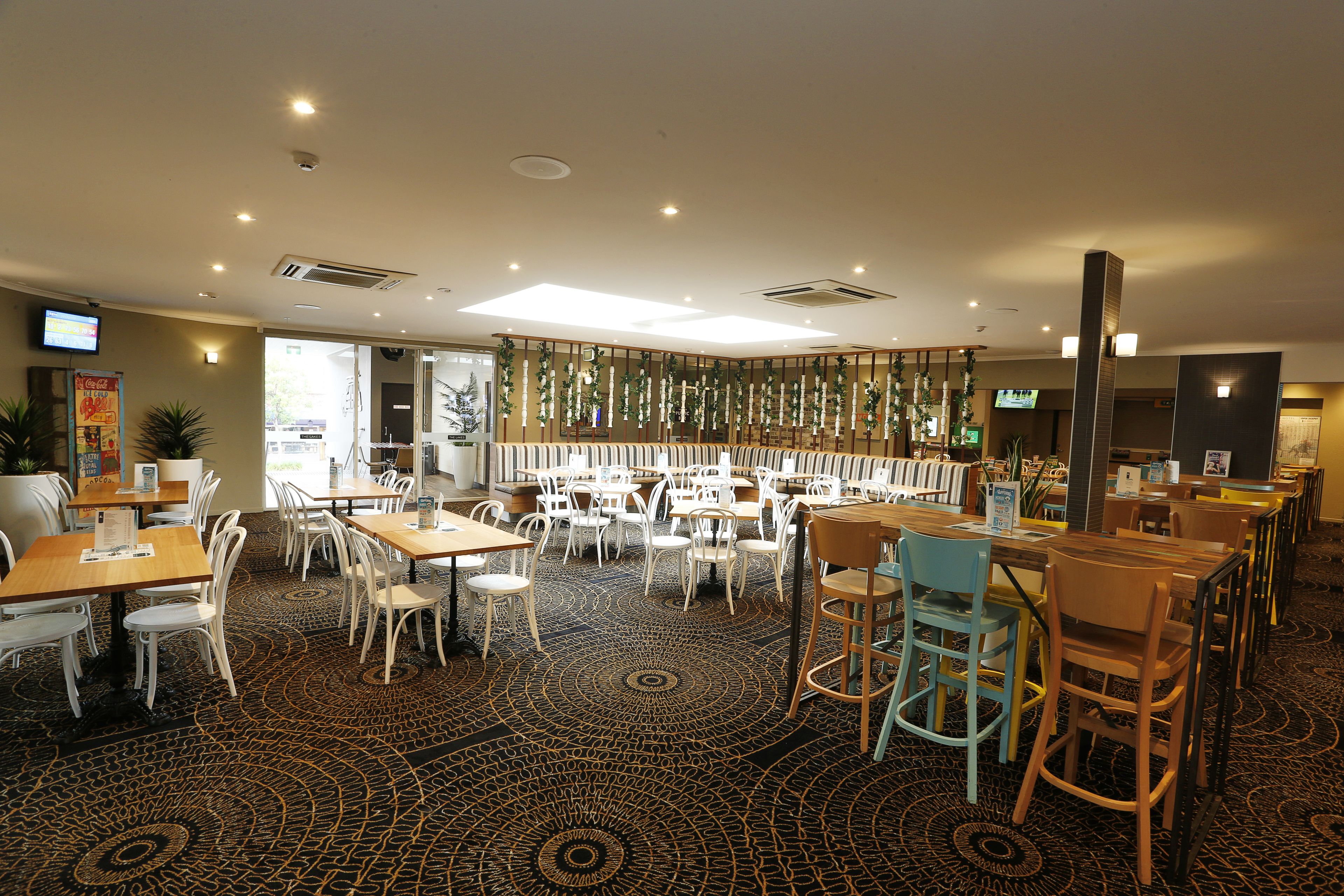 A spacious restaurant with multiple tables and chairs, a patterned carpet, and a modern ceiling design.