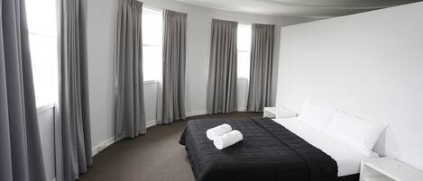 Habitación de hotel con cama, mesita de noche blanca y ventilador de techo.