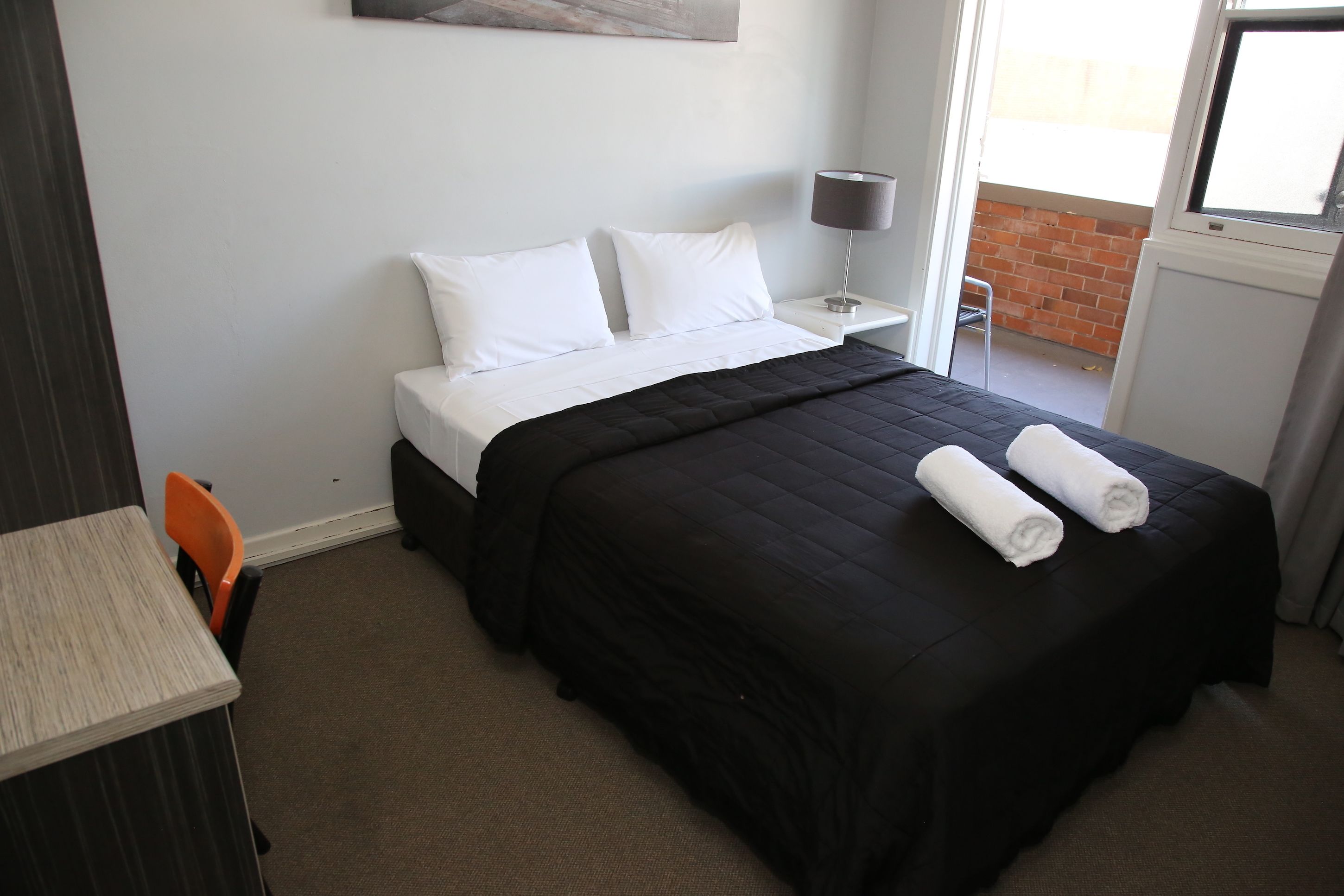 A hotel room with a bed, a nightstand, a lamp, a chair, and a table.
