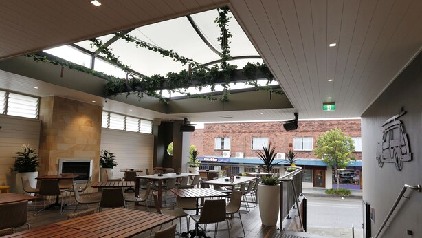 An indoor patio area with wooden tables and chairs, a fireplace, and hanging plants. - The Lakes Hotel (The Entrance)