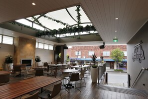 An indoor patio area with wooden tables and chairs, a fireplace, and hanging plants.