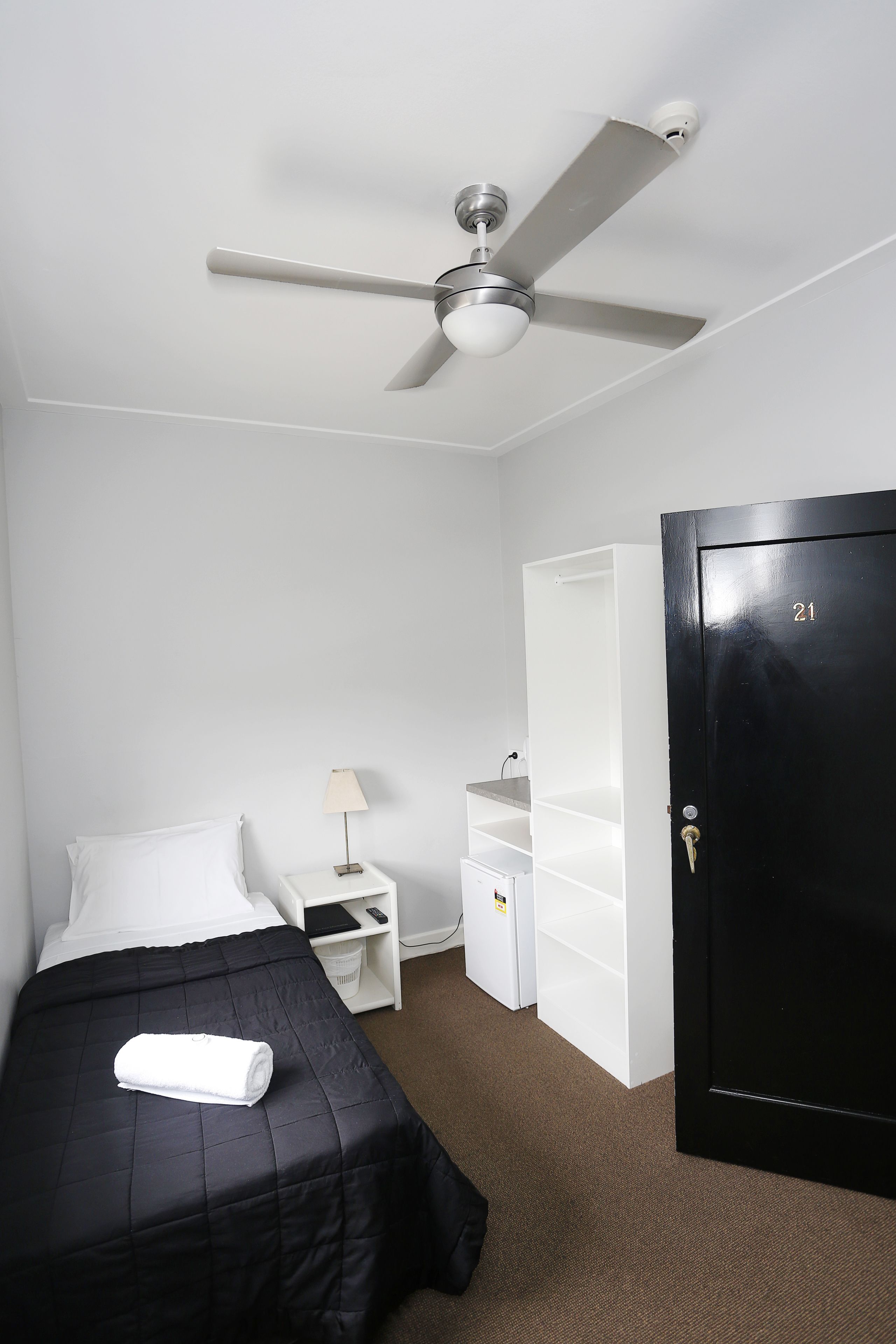 A hotel room with a bed, a nightstand, a lamp, a wardrobe, and a ceiling fan.
