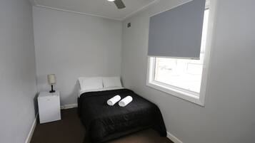 A small, neatly arranged bedroom with a single bed, a nightstand, a lamp, and a ceiling fan.