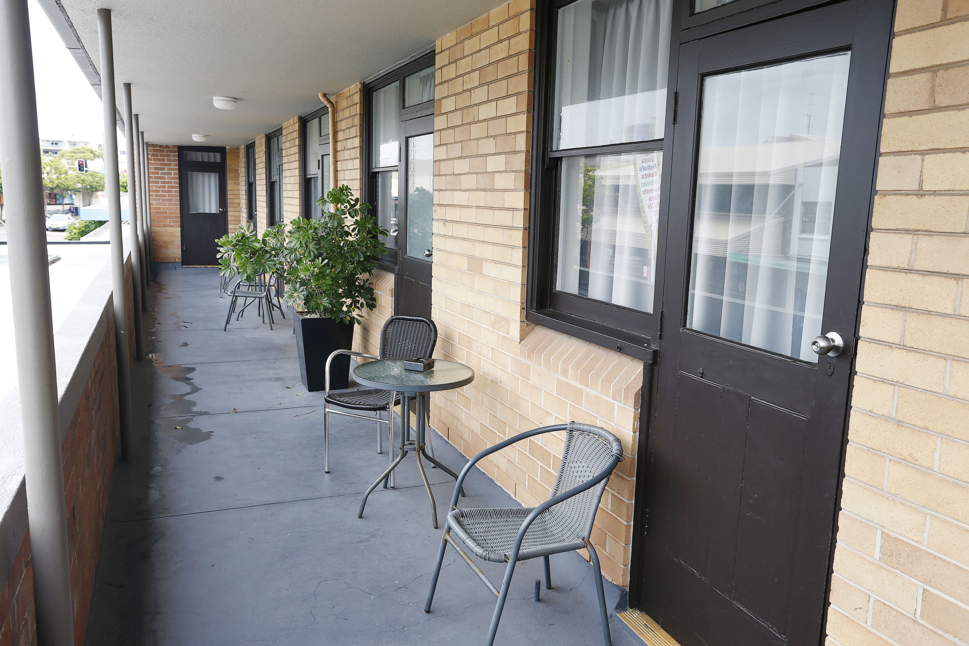 A covered outdoor area with a brick wall, a door, and two metal chairs with a table.