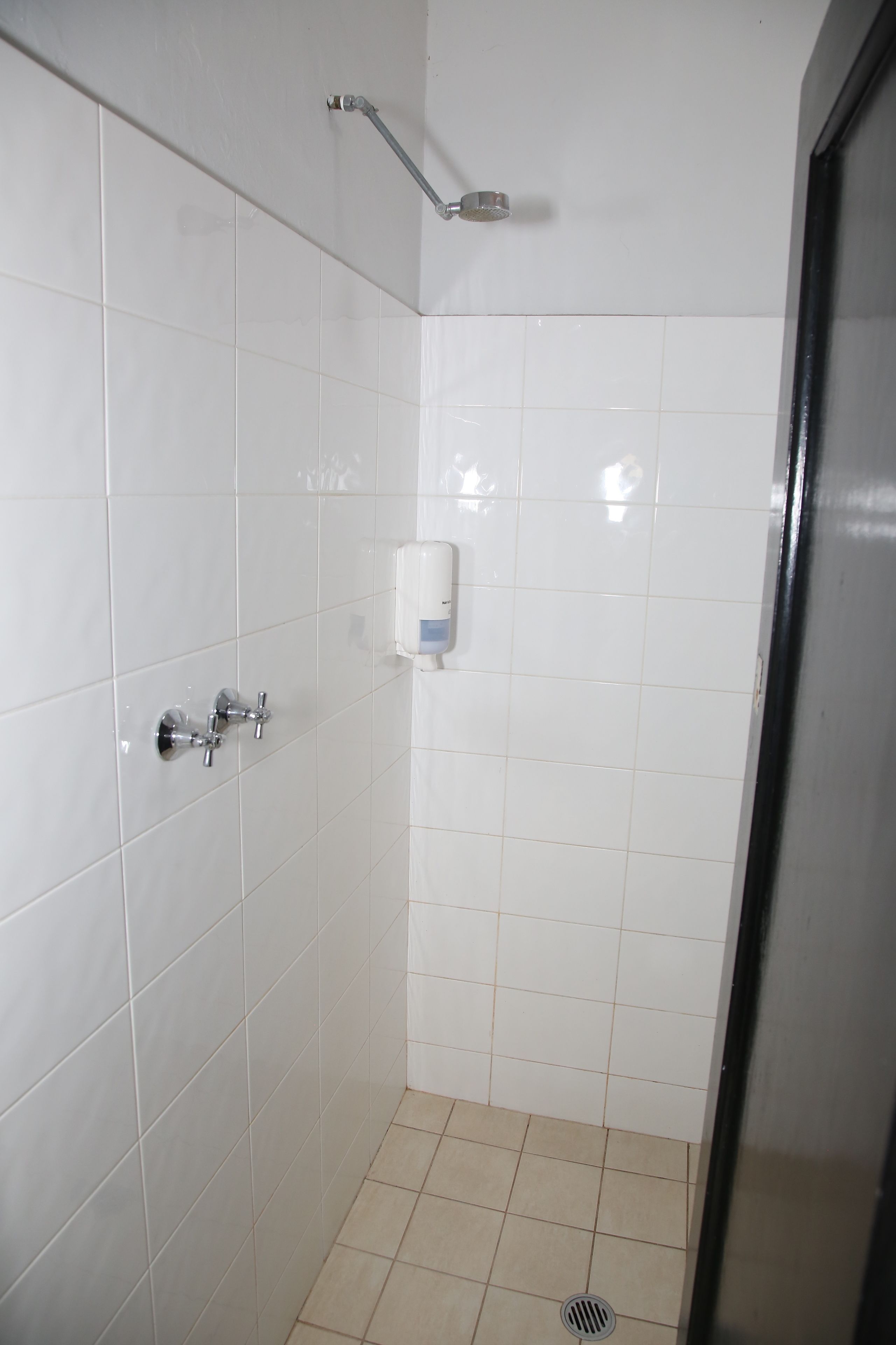 A small, tiled shower area with a handheld showerhead and a soap dispenser mounted on the wall.