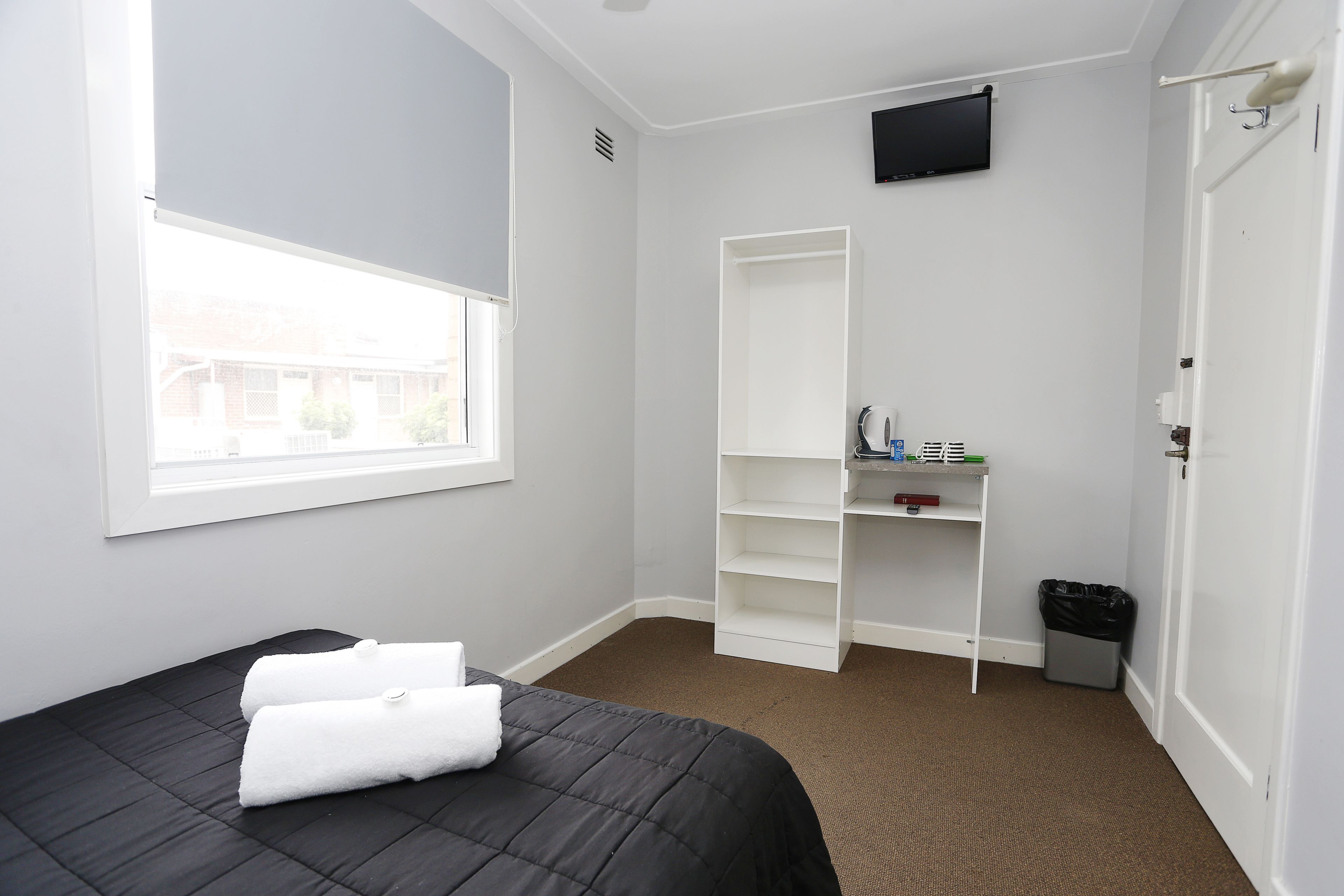 Ein Hotelzimmer mit Bett, Fenster, Fernseher, weißem Wäscheschrank und Mülleimer.