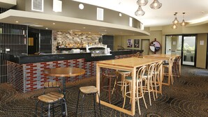 A modern bar area with a brick wall, a wooden bar counter, and a seating area with wooden tables and chairs. - The Lakes Hotel (The Entrance)