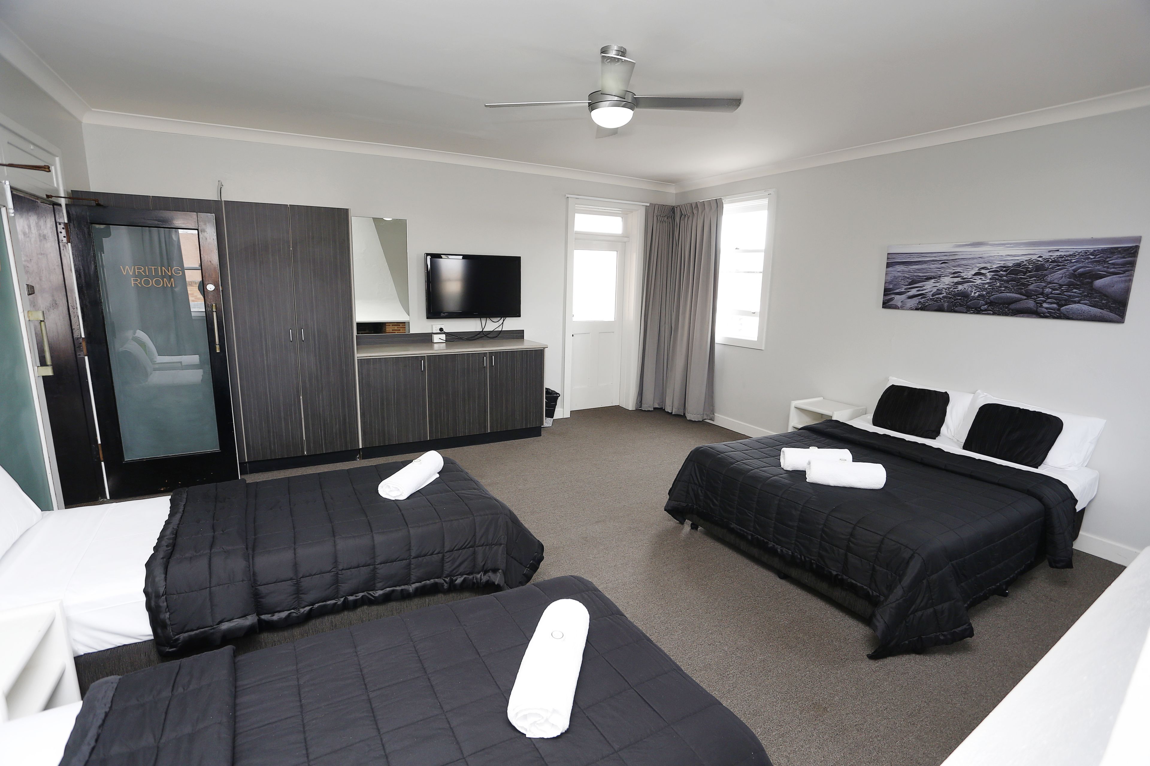 Ein Hotelzimmer mit zwei Betten, einem Fernseher, einem Schreibtisch und einem Bild an der Wand.