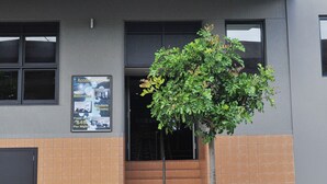 A building with a sign reading "THE LAKES" above the entrance. There is a tree in front of the building. - The Lakes Hotel (The Entrance)