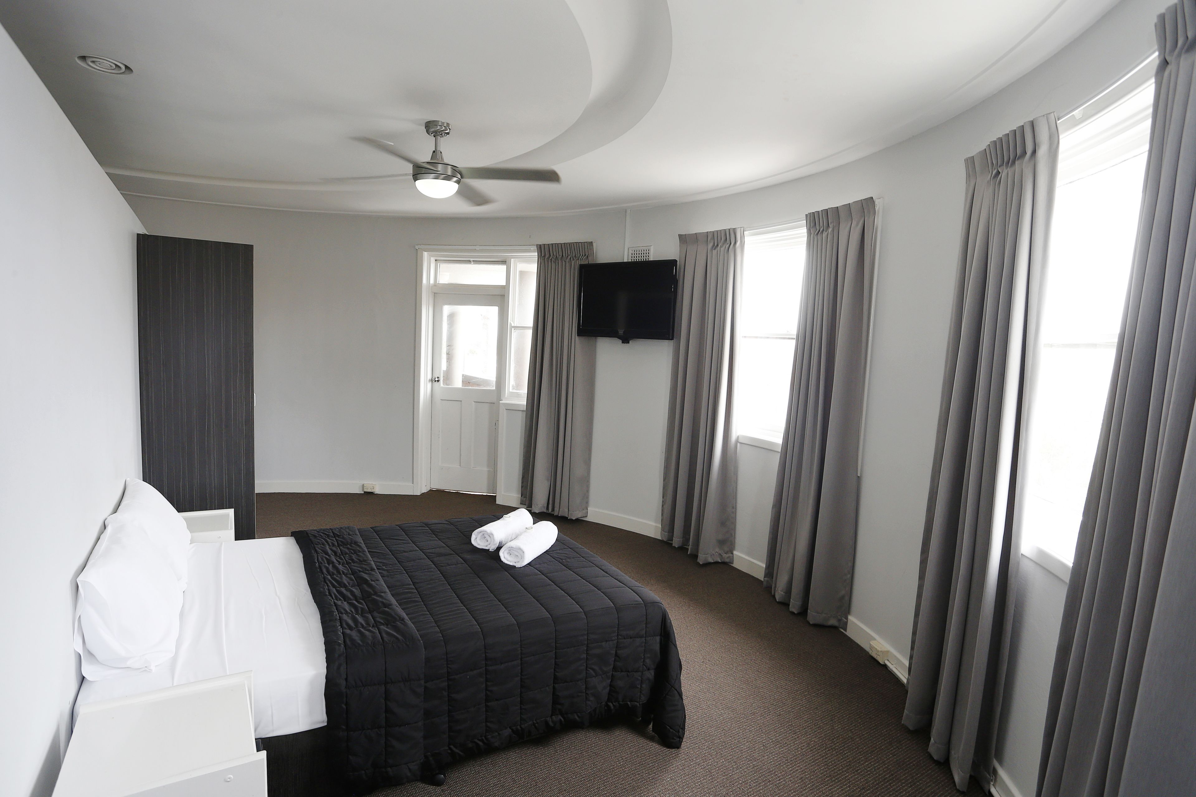 A hotel room with a bed, a flat-screen TV mounted on the wall, and a ceiling fan.