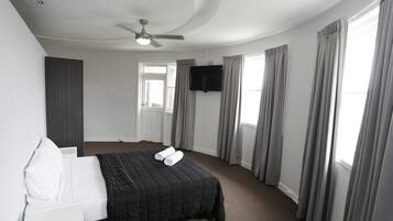 A hotel room with a bed, a flat-screen TV mounted on the wall, and a ceiling fan.