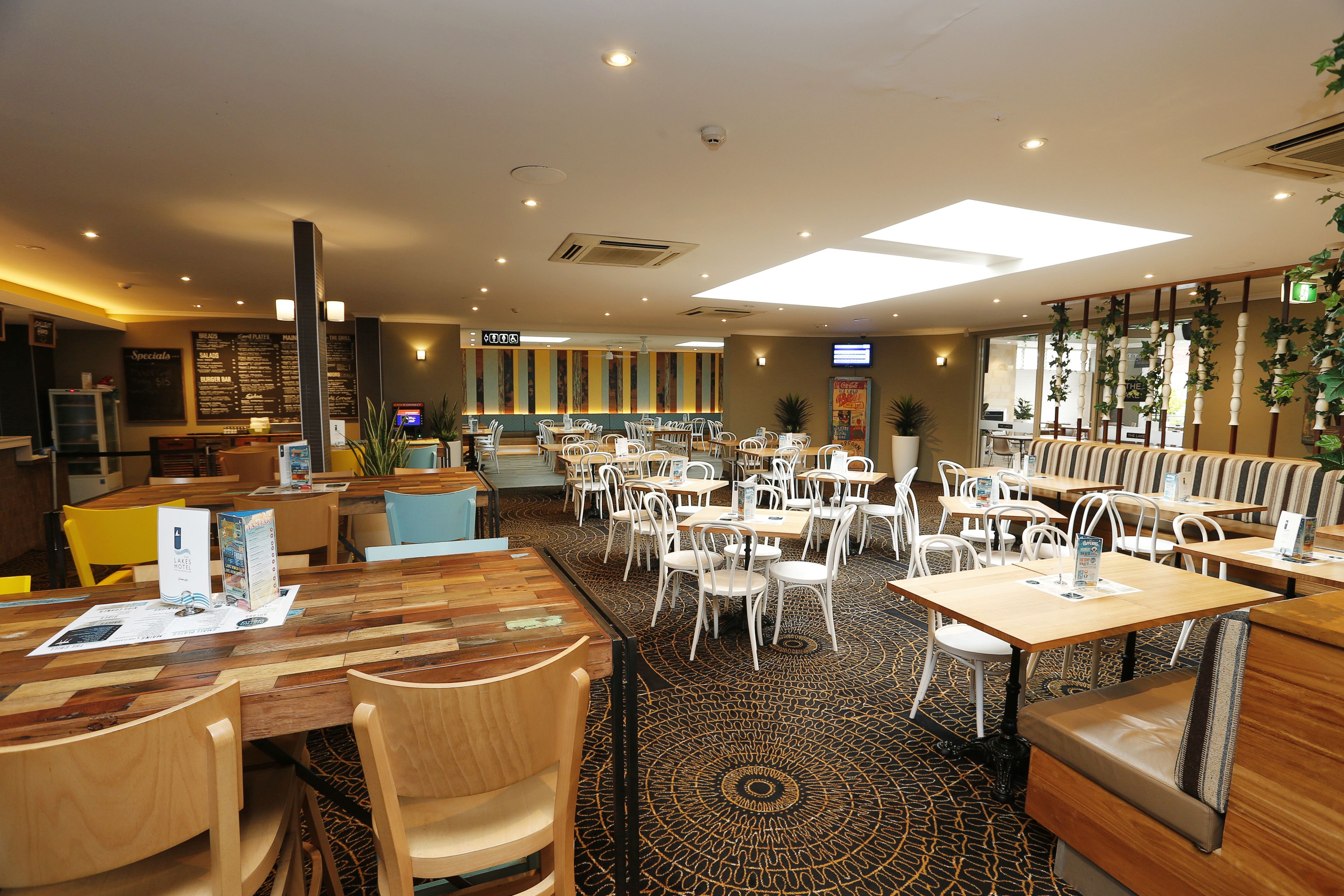 A restaurant with multiple dining tables and chairs, a menu board, and a counter area.