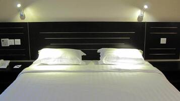 A hotel room with a bed, two bedside tables, a nightstand, a framed picture on the wall, and two wall-mounted lamps.