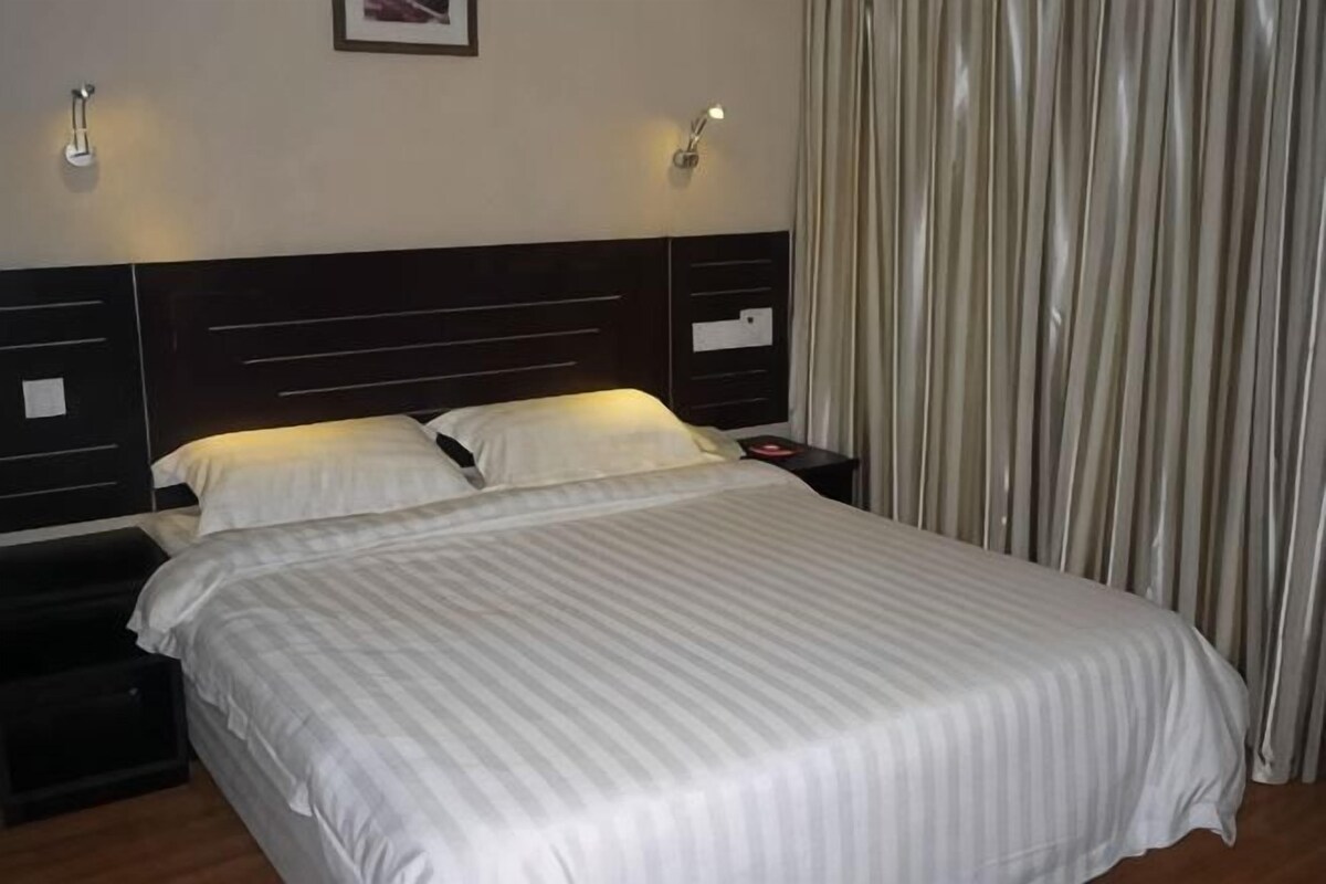 Una habitación de hotel con cama, mesitas de noche y una cortina.
