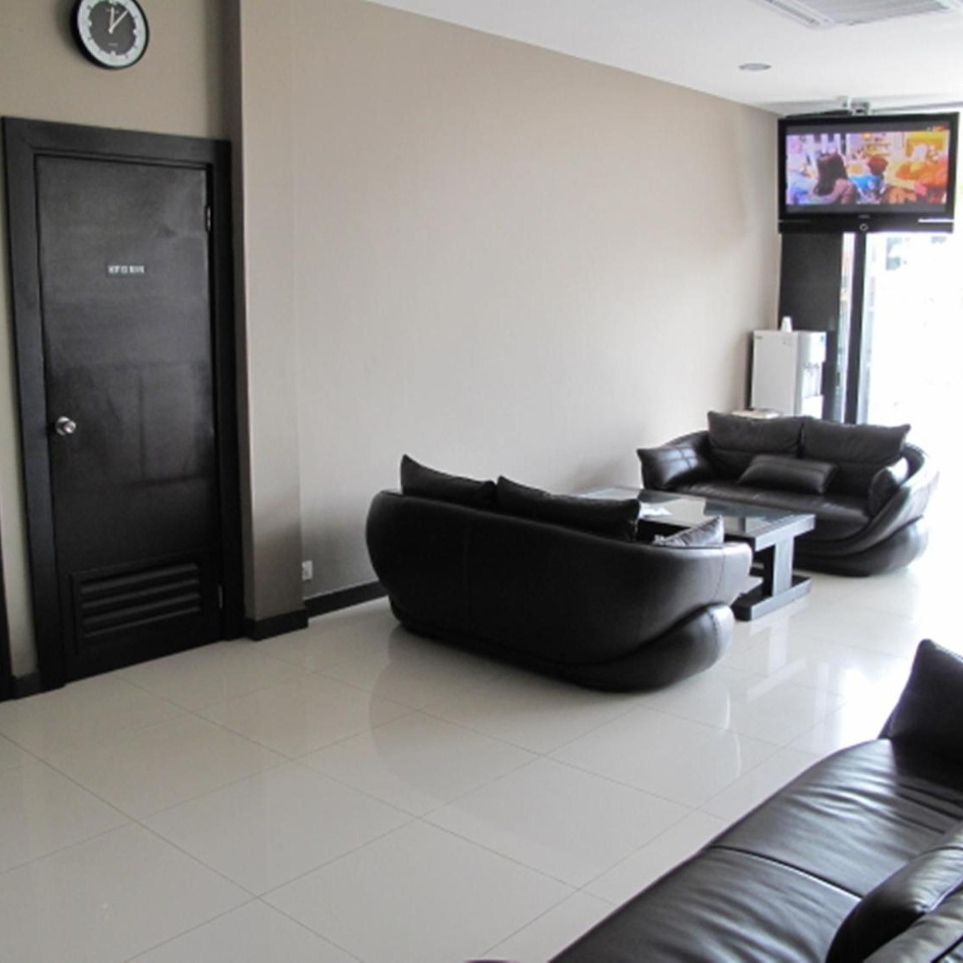 A modern living room with a black sofa set, a flat-screen TV mounted on the wall, and a door with a clock.