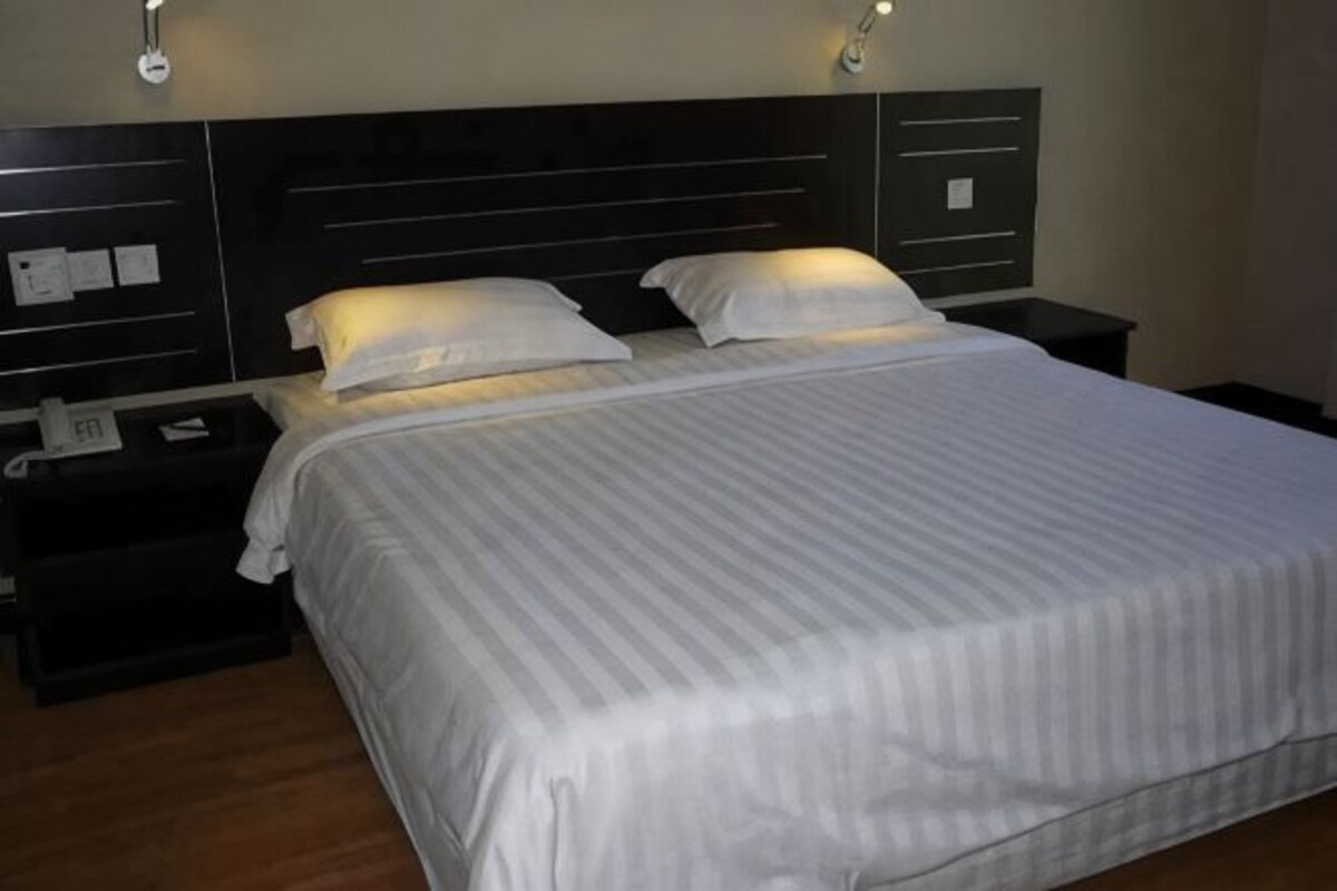 A hotel room with a large bed, two bedside tables, and wall-mounted lighting.
