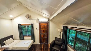 Een slaapkamer met een bed, een stoel, een raam met uitzicht op groen, en een plafondventilator.